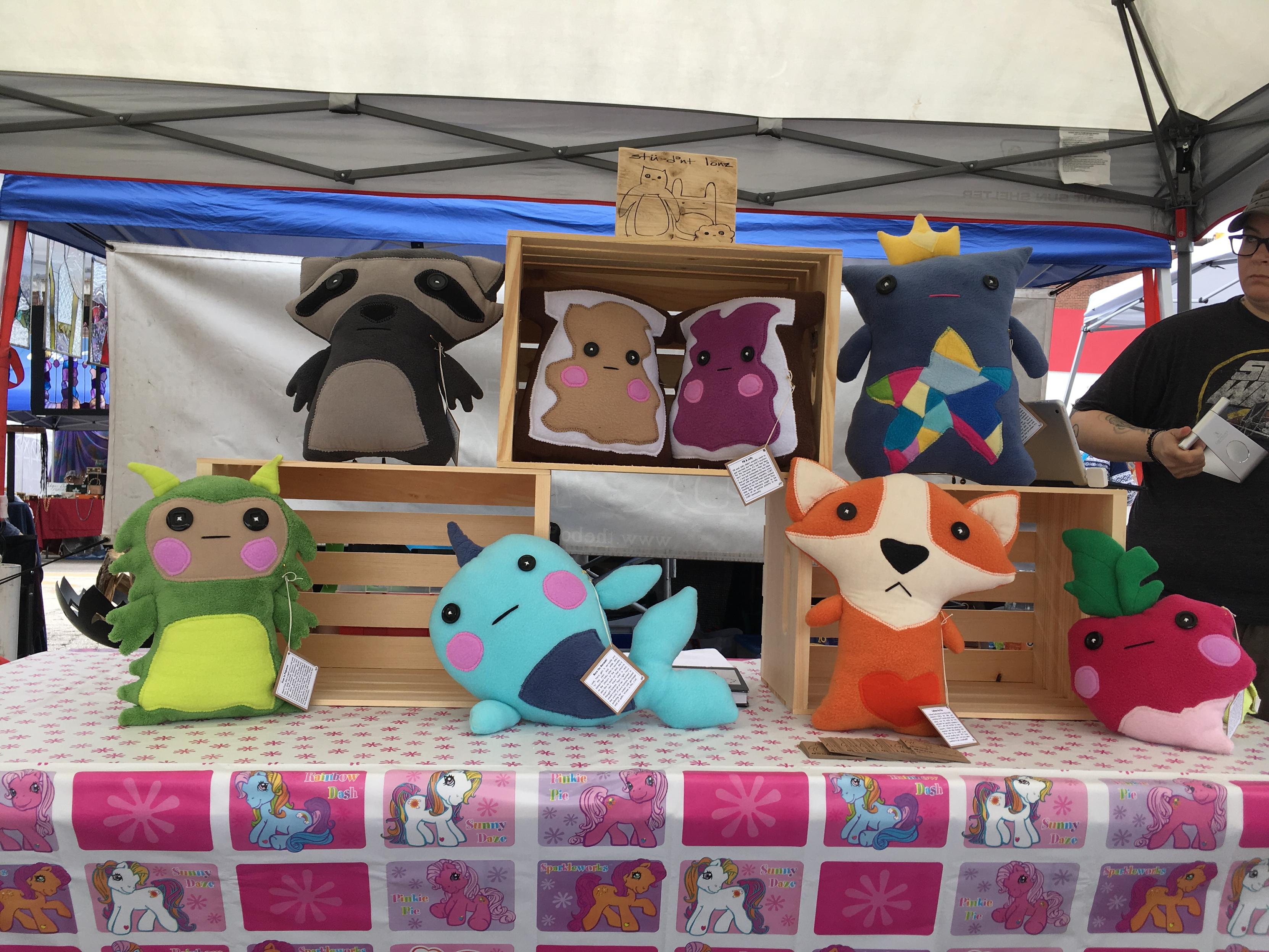 plushies of: a kid in dino pajamas, a fox, a narwhal, a turnip, a racoon, a lost sock fairy queen, and a peanut butter and jelly sandwich. also pictured is a half-shot of my younger sibling, who encouraged me to join them.